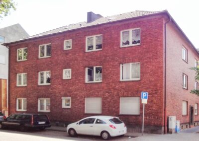 Immobilienmakler und Hausverwaltung Oberhausen - Bild eines Mehrfamilienhauses in Oberhausen, an einer Kreuzung, über Ecke aufgenommen mit roten Ziegel.